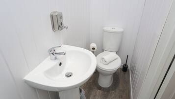 Un baño pequeño y blanco con lavamanos, inodoro y dispensador de papel higiénico.