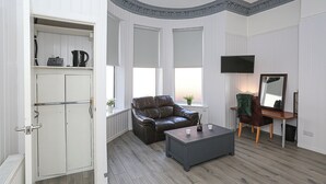 Un salon moderne avec un canapé en cuir, une table basse, un téléviseur et un bureau agrémenté d’un miroir.