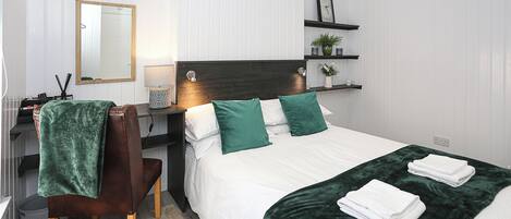 A neatly arranged bedroom with a bed, bedside table, chair, and a mirror.