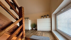 Un escalier en bois avec une rampe, une commode blanche agrémentée de plantes en pot et une fenêtre avec du verre texturé.