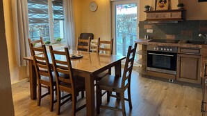 Un coin repas avec une table et des chaises en bois, une horloge au mur et une cuisine équipée d’une cuisinière et de placards.