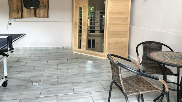Une pièce avec une table de ping-pong, des chaises en osier, un meuble en bois et un luminaire fixé au mur.