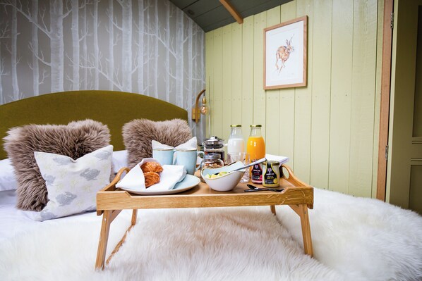A cozy bedroom with a bed, fluffy pillows, a wooden bedside table with breakfast items, and a wall with a tree pattern. - Lympstone Manor Hotel (Exmouth)