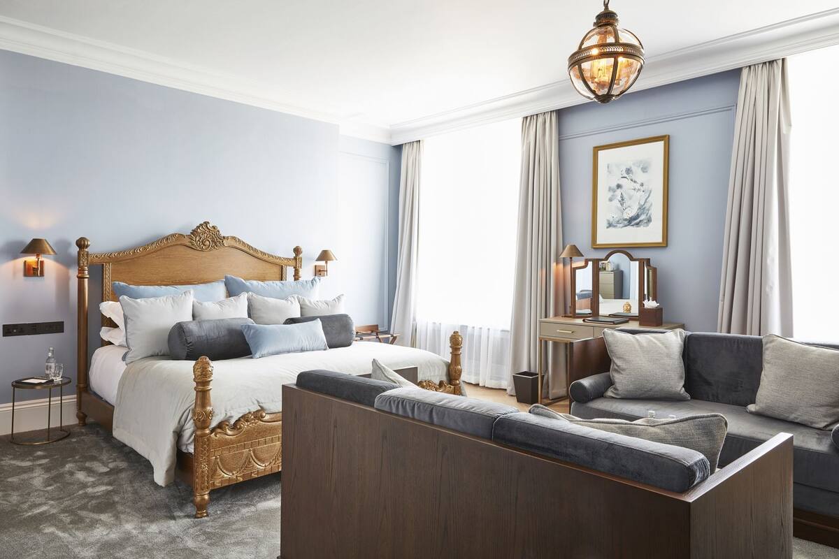 A bedroom with a large bed, a sofa, a bedside table, a lamp, and a window with curtains.