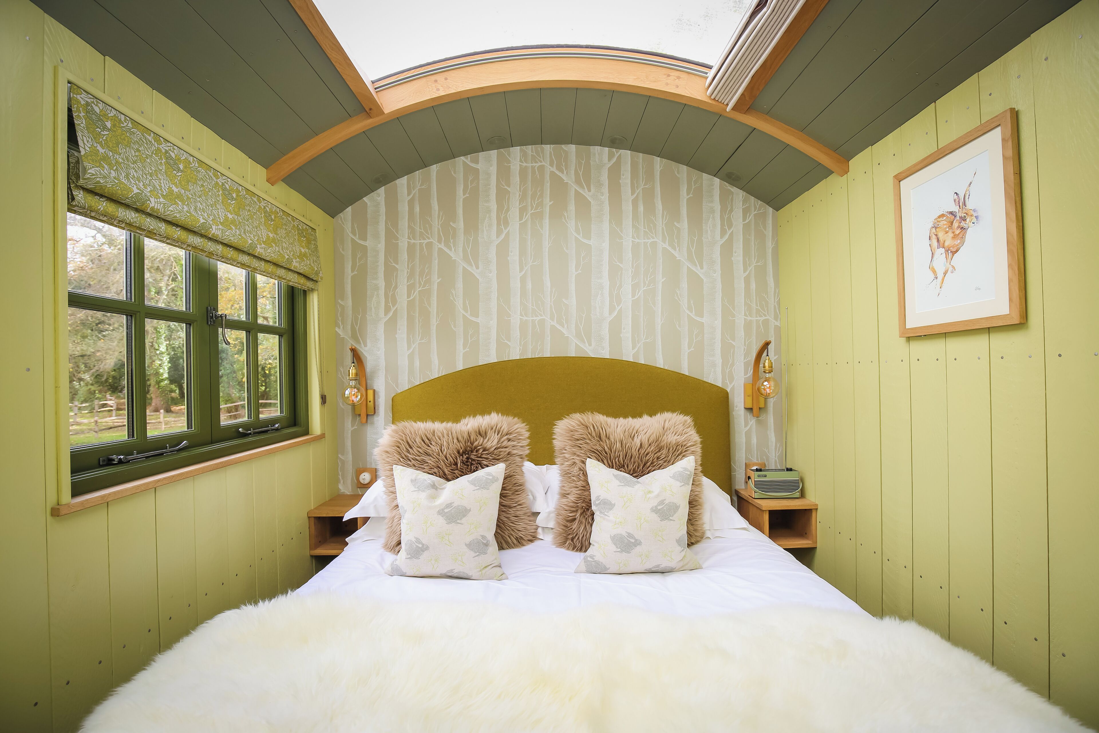 A room with a bed, two nightstands, a window with a view, and a framed picture on the wall.