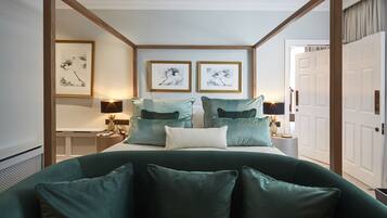 A bedroom with a four-poster bed, two framed artworks on the wall, and a nightstand with a lamp.