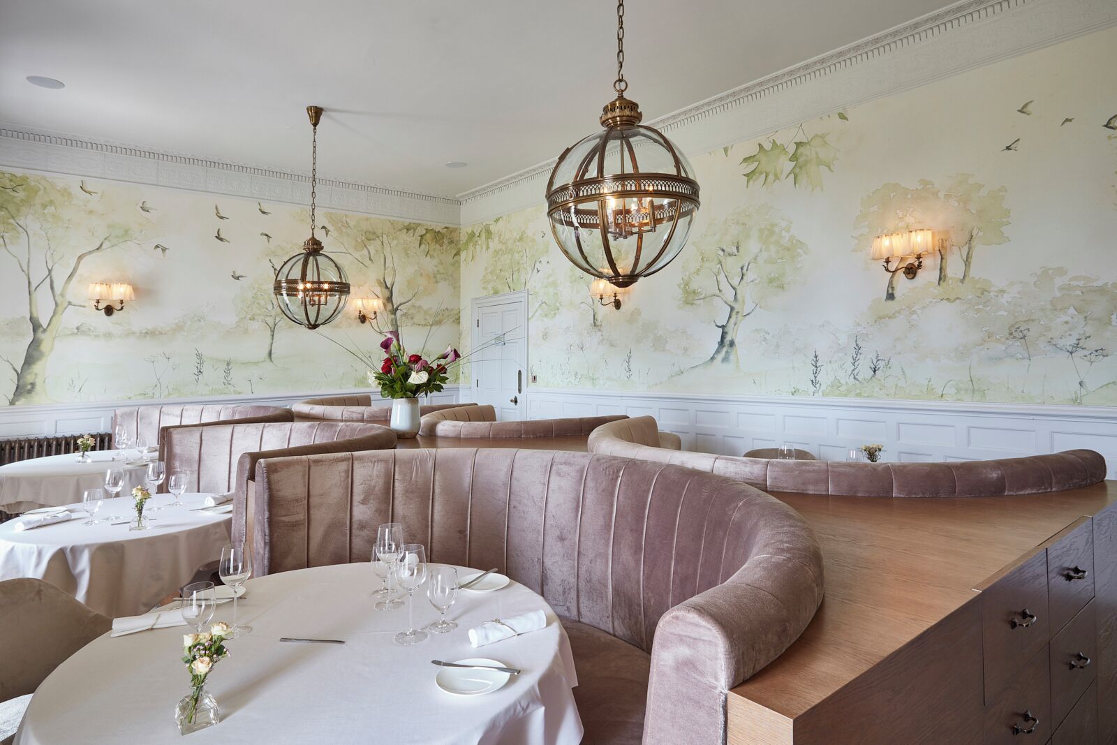 Un comedor con mesas redondas, asientos acolchados y murales decorativos.