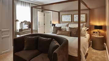 A four-poster bed with a headboard, a brown sofa, a bedside table with a lamp, and a framed artwork on the wall.