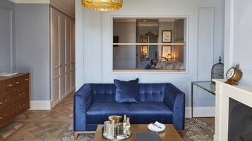 A living room with a blue sofa, a wooden coffee table with bottles, a fireplace, and a large window with a mirror.