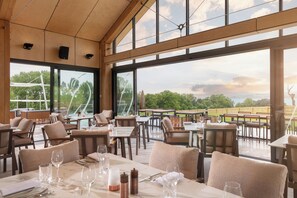 An outdoor dining area with tables and chairs, large windows, and a view of the landscape. - Lympstone Manor Hotel (Exmouth)