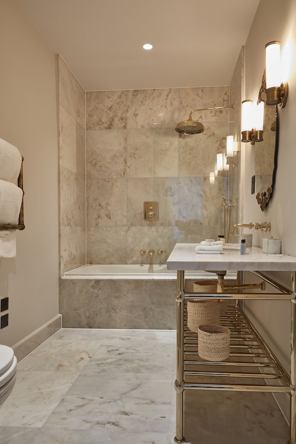 A modern bathroom with a marble shower, a white sink, and gold fixtures.