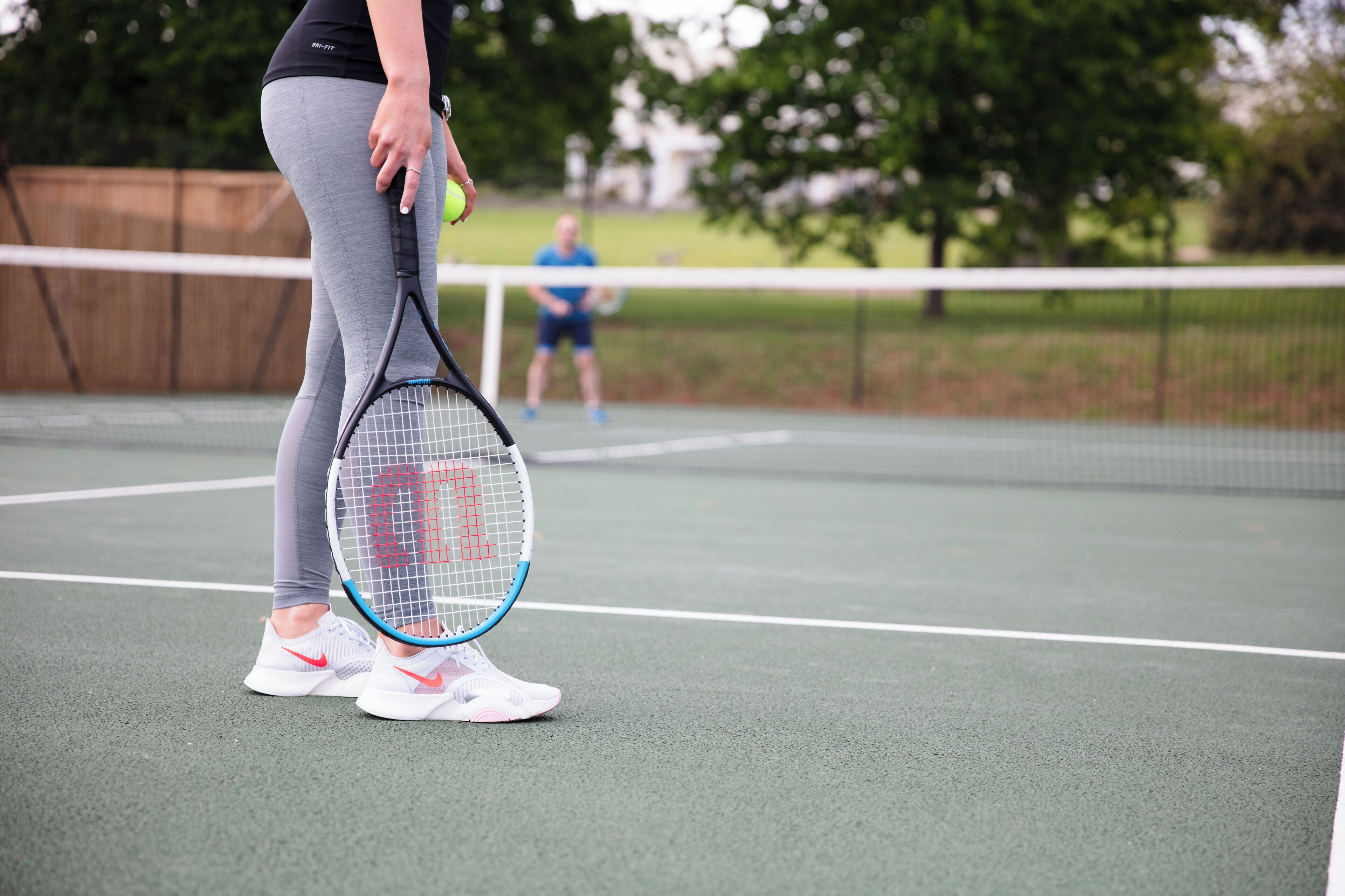 A tennis court with a net in the middle, a player holding a tennis racket, and another player in the background.