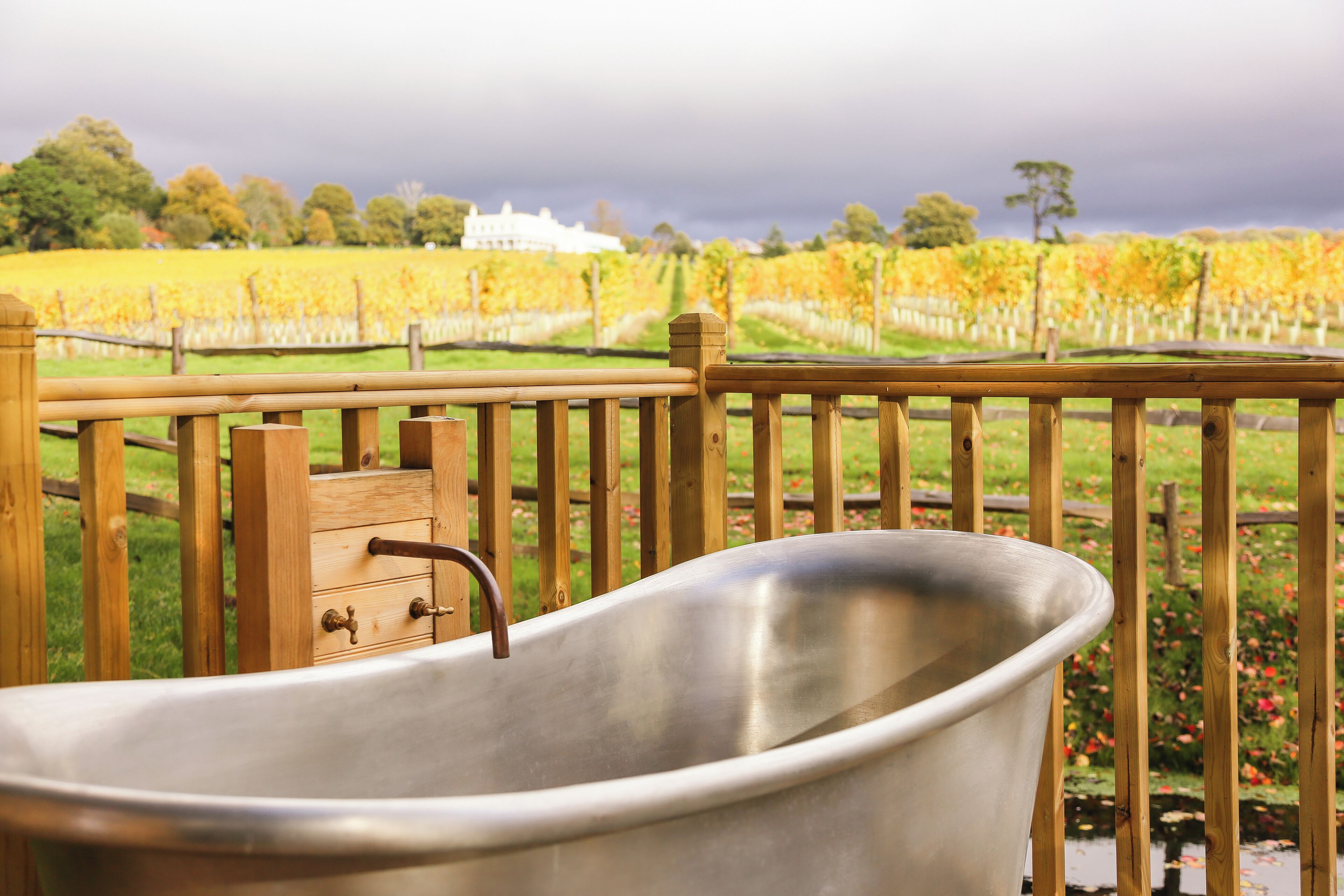 A metal bathtub on a wooden deck with a vineyard and a white building in the background.