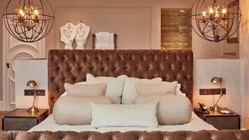 A bedroom with a tufted headboard, two bedside tables with lamps, and a chandelier.