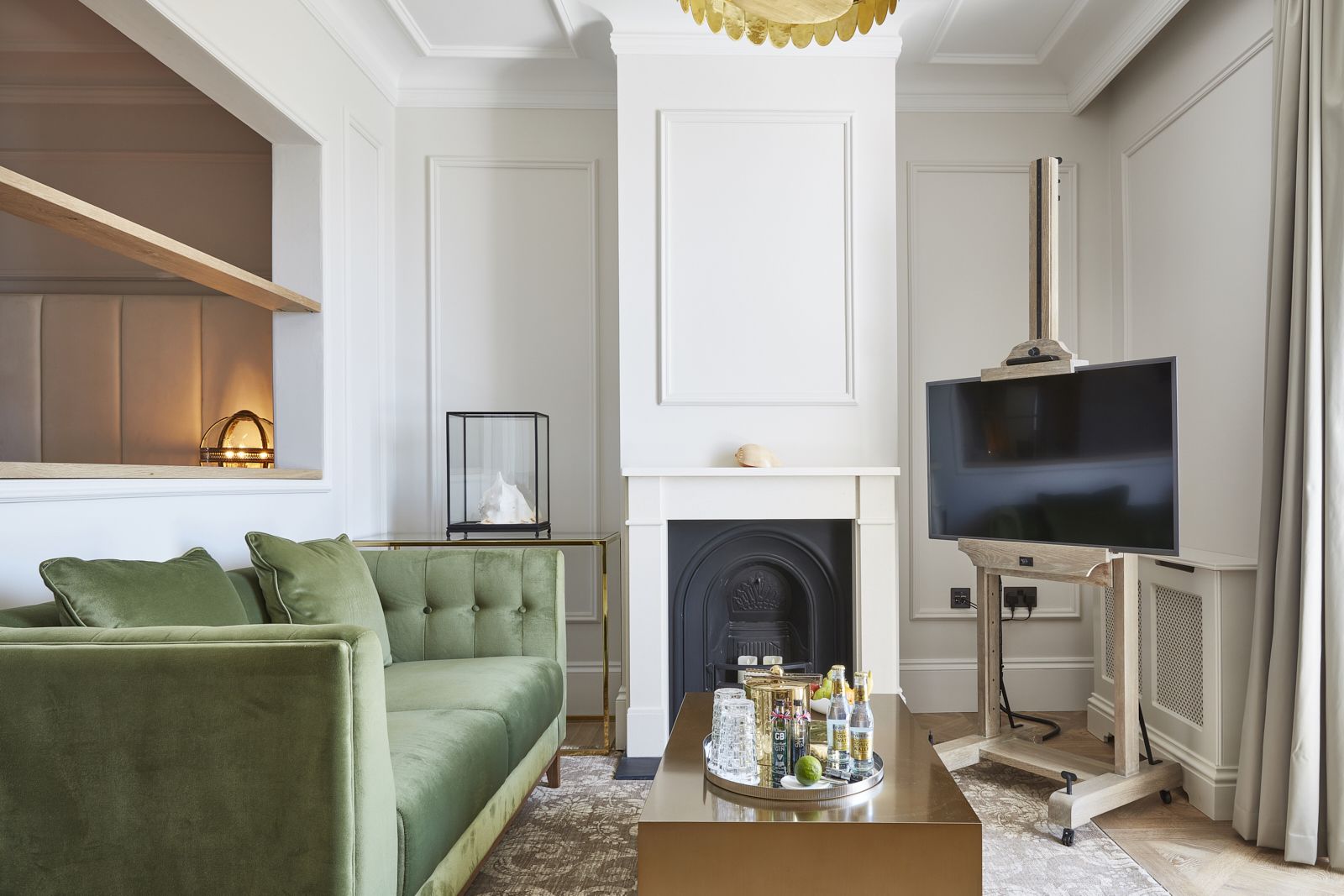 Una sala de estar con un sofá verde, una chimenea, un televisor y una mesa de centro con varios objetos.