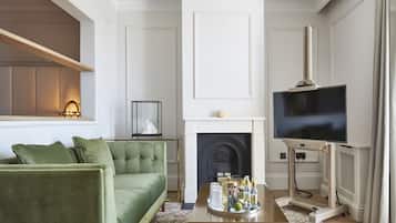 Una sala de estar con un sofá verde, una chimenea, un televisor y una mesa de centro con varios objetos.