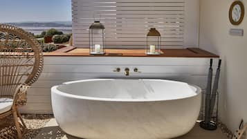 A large freestanding bathtub in a sunlit bathroom with a view of the sea.