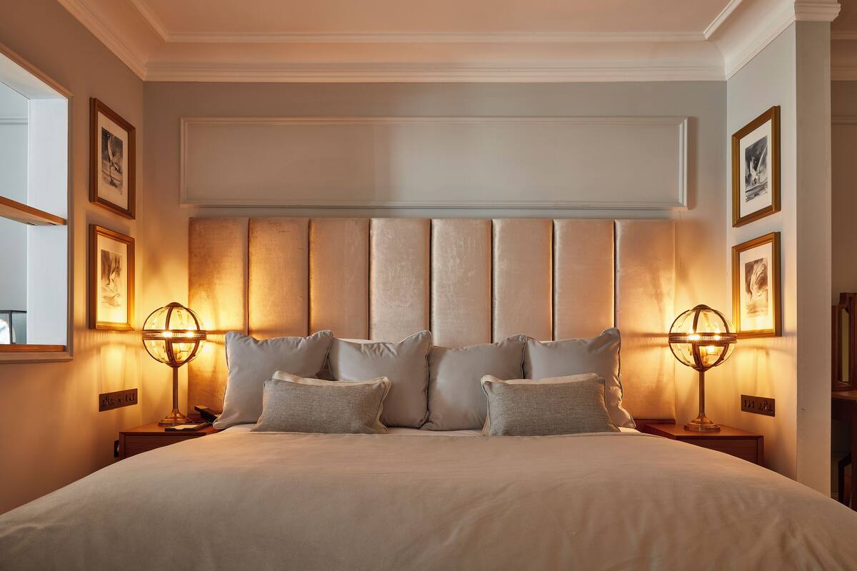 A large bed with a padded headboard, two bedside lamps, and framed pictures on the walls.