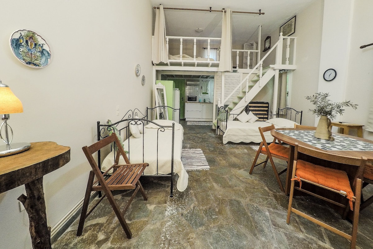 A cozy room with a bed, a table with chairs, a lamp, and a staircase leading to an upper level.