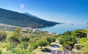 A coastal landscape with a clear view of the sea, a mountain in the background, and a small settlement with buildings and greenery. - Kypri Apartments (Andros)