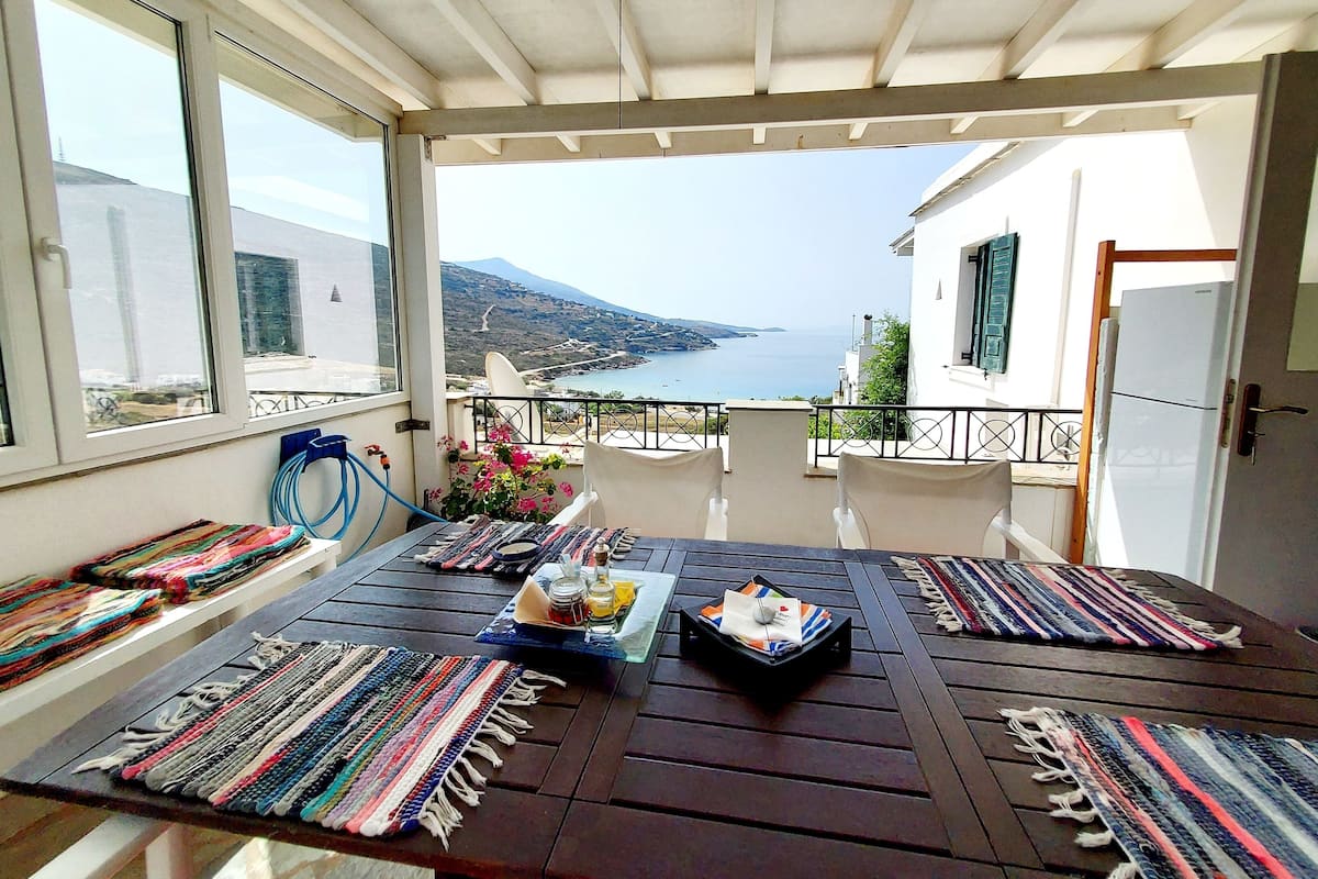 A balcony with a view of the sea, a table with a rug, and a refrigerator.