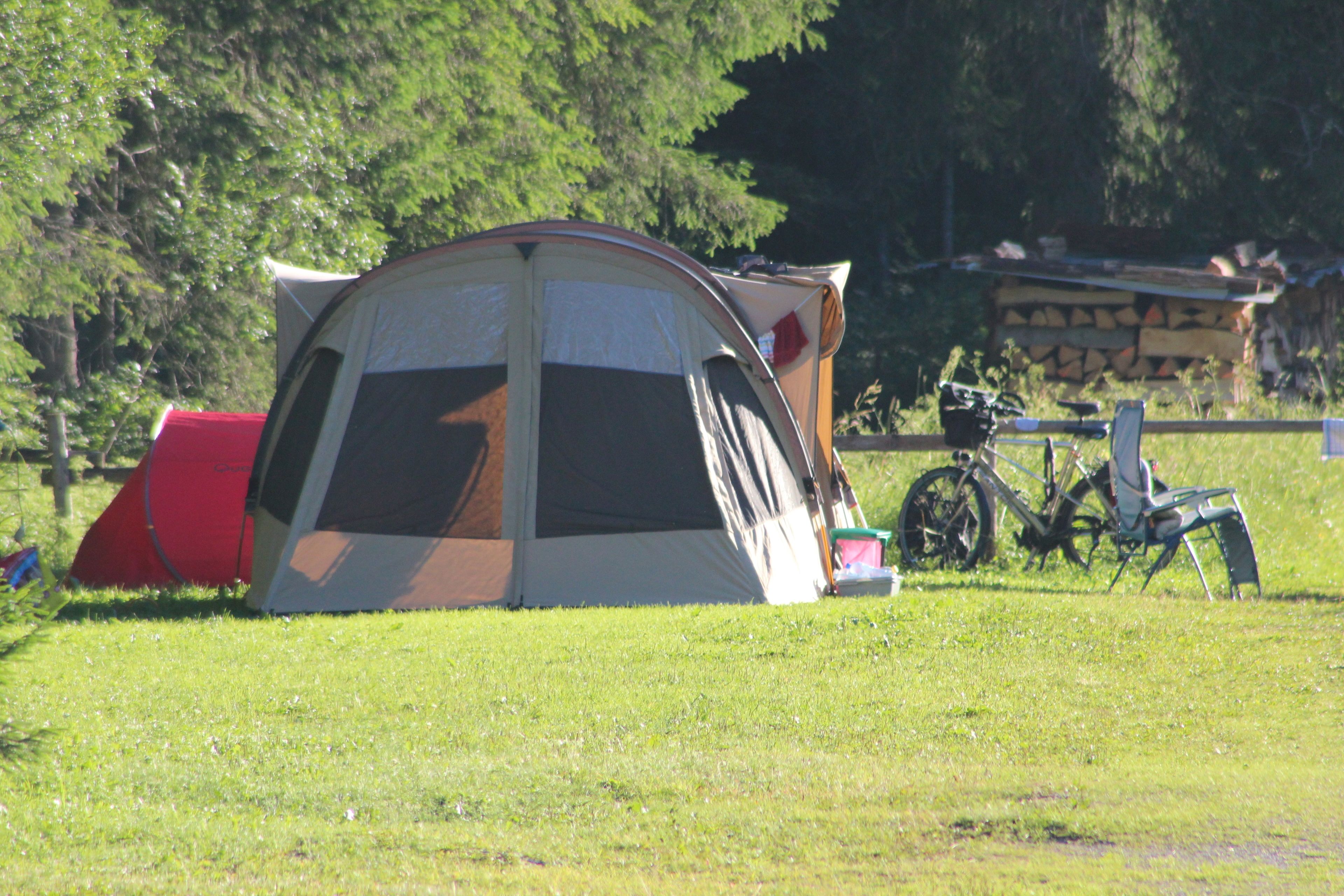 A camping tent in a grassy field with trees in the background.