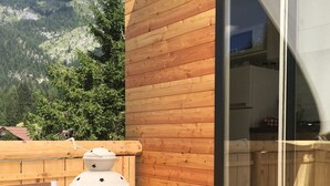 Um deck de madeira com uma mesa e um candeeiro, com vista para uma paisagem montanhosa.