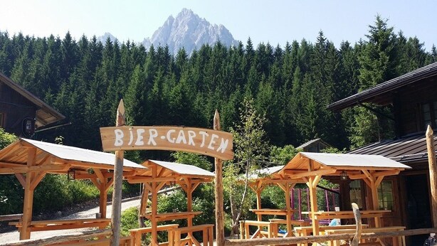 A wooden outdoor seating area with a sign reading "BIER-CARTEN" and a mountain in the background.
