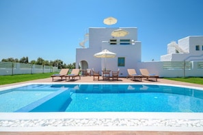 A swimming pool with lounge chairs and umbrellas, surrounded by a white building with a staircase.