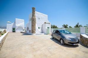 A modern white building with a stone column, a car parked in front, and a clear blue sky.