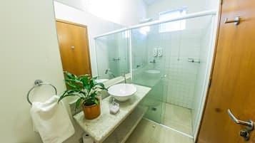 A bathroom with a glass-enclosed shower, a sink with a marble countertop, a potted plant, and a towel rack.