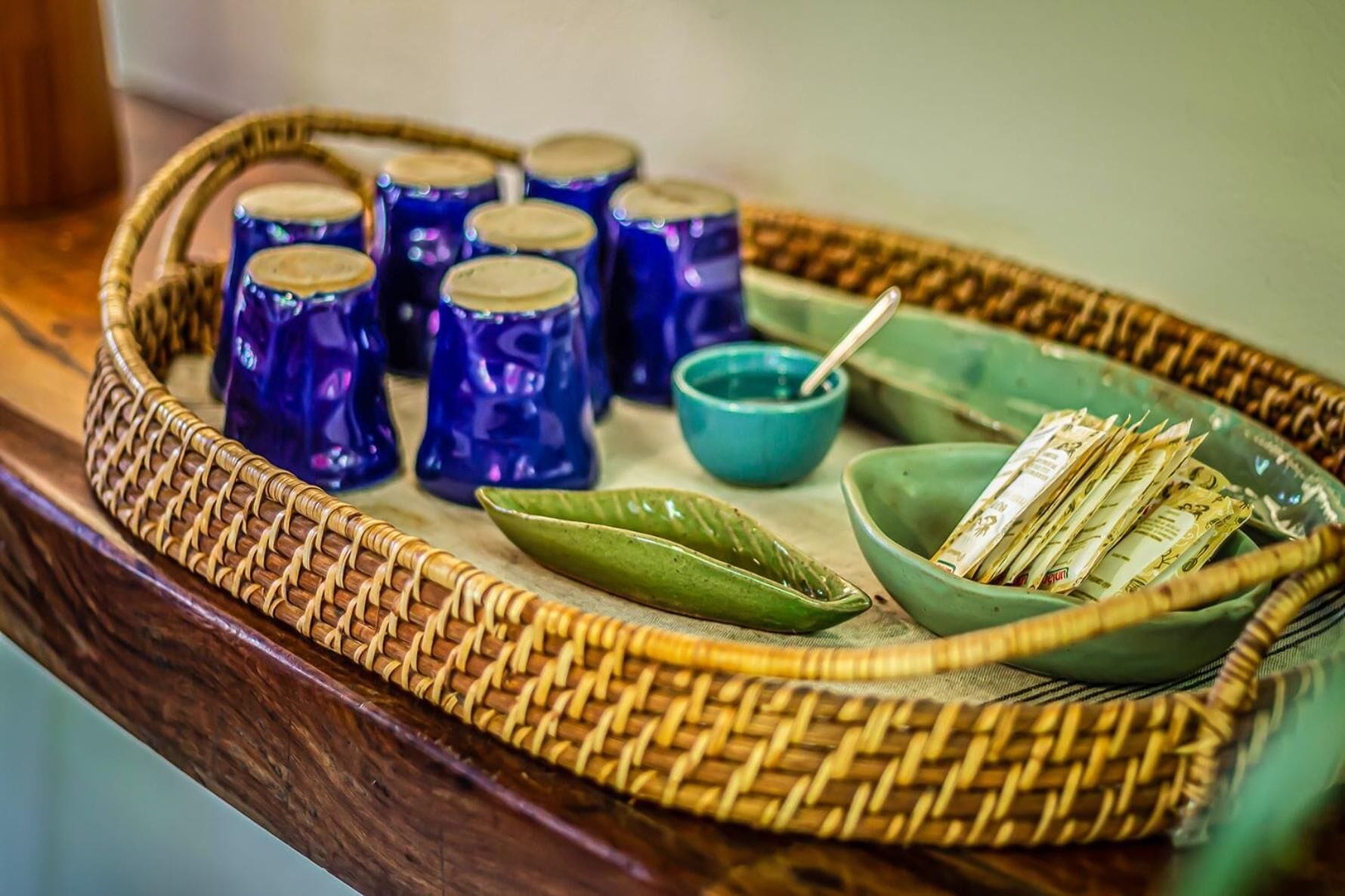 A woven basket containing blue glass bottles, a green leaf, a teal bowl with a spoon, and a bowl of currency notes.