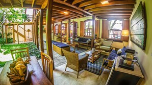 A cozy lounge area with wooden furniture, a dining table with fruit, and a view of the garden. - Pousada Ipê (São Sebastião)