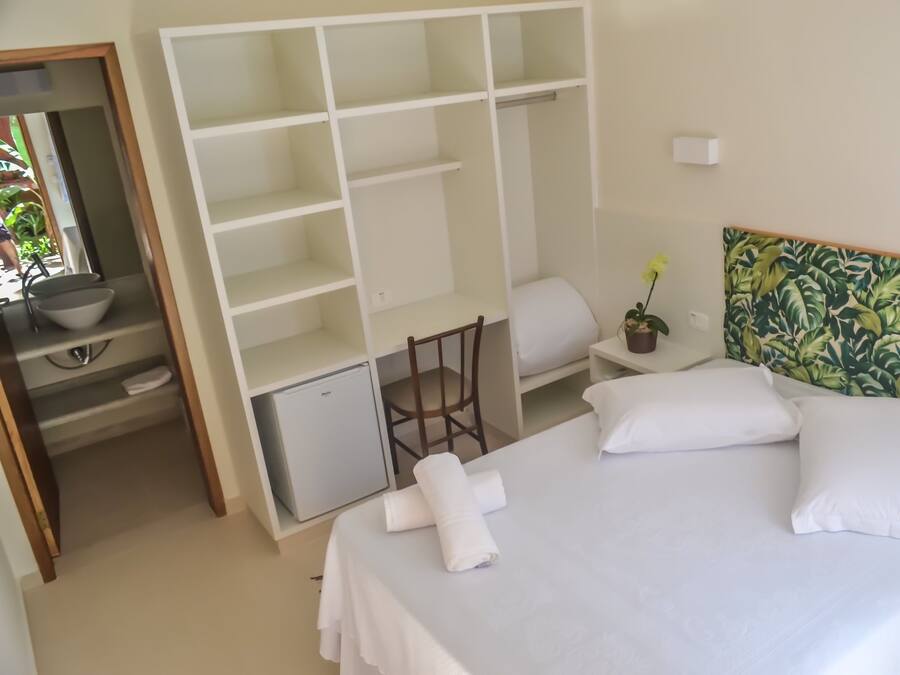 A hotel room with a bed, a desk, a chair, a small refrigerator, and a wardrobe.