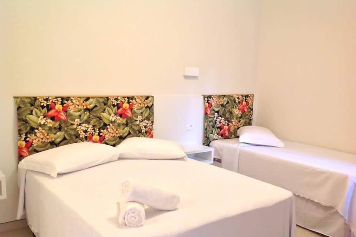 A hotel room with two single beds, each with white bedding and a floral headboard. A rolled towel is placed on the bed in the foreground.