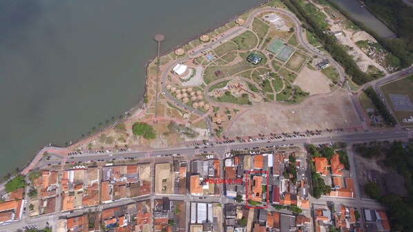 Vista aérea de una zona costera con un puerto deportivo, un parque con instalaciones deportivas y una área residencial con casas adosadas.