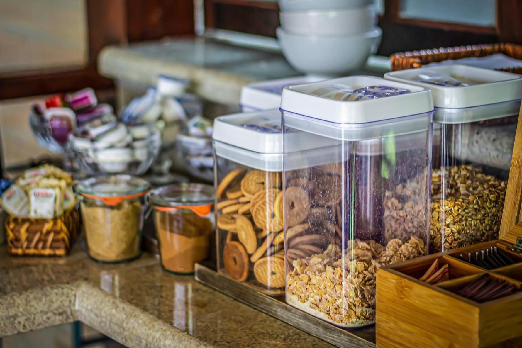 Una encimera de cocina con diversos alimentos en recipientes, entre ellos frascos de especias y una caja de madera con utensilios.
