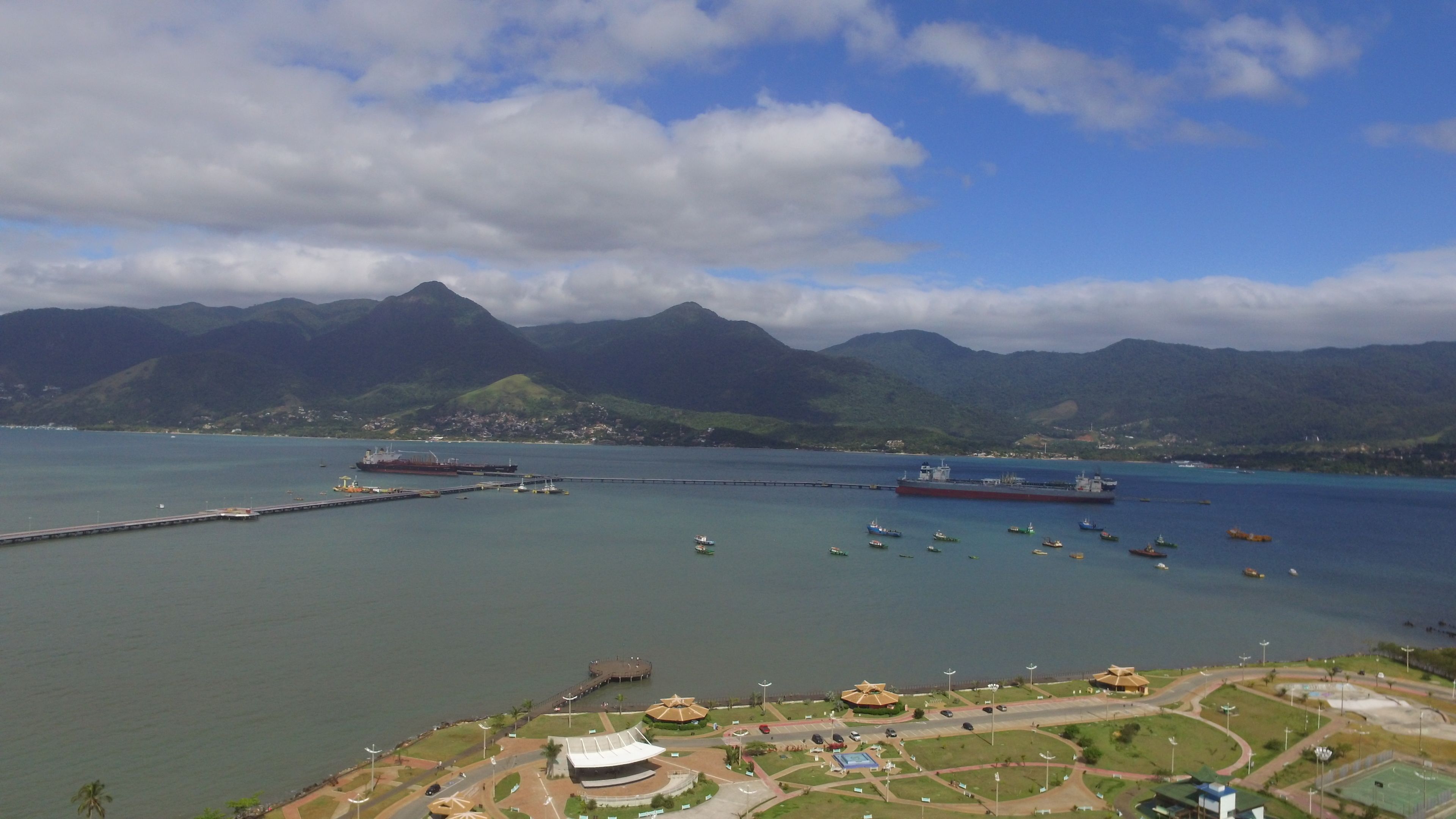 Un paisaje costero con una extensa masa de agua, varios barcos y montañas al fondo.