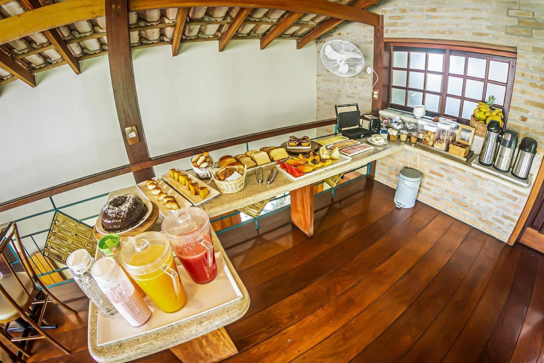 A breakfast buffet with various food items and beverages, a fan, and a window with a view.