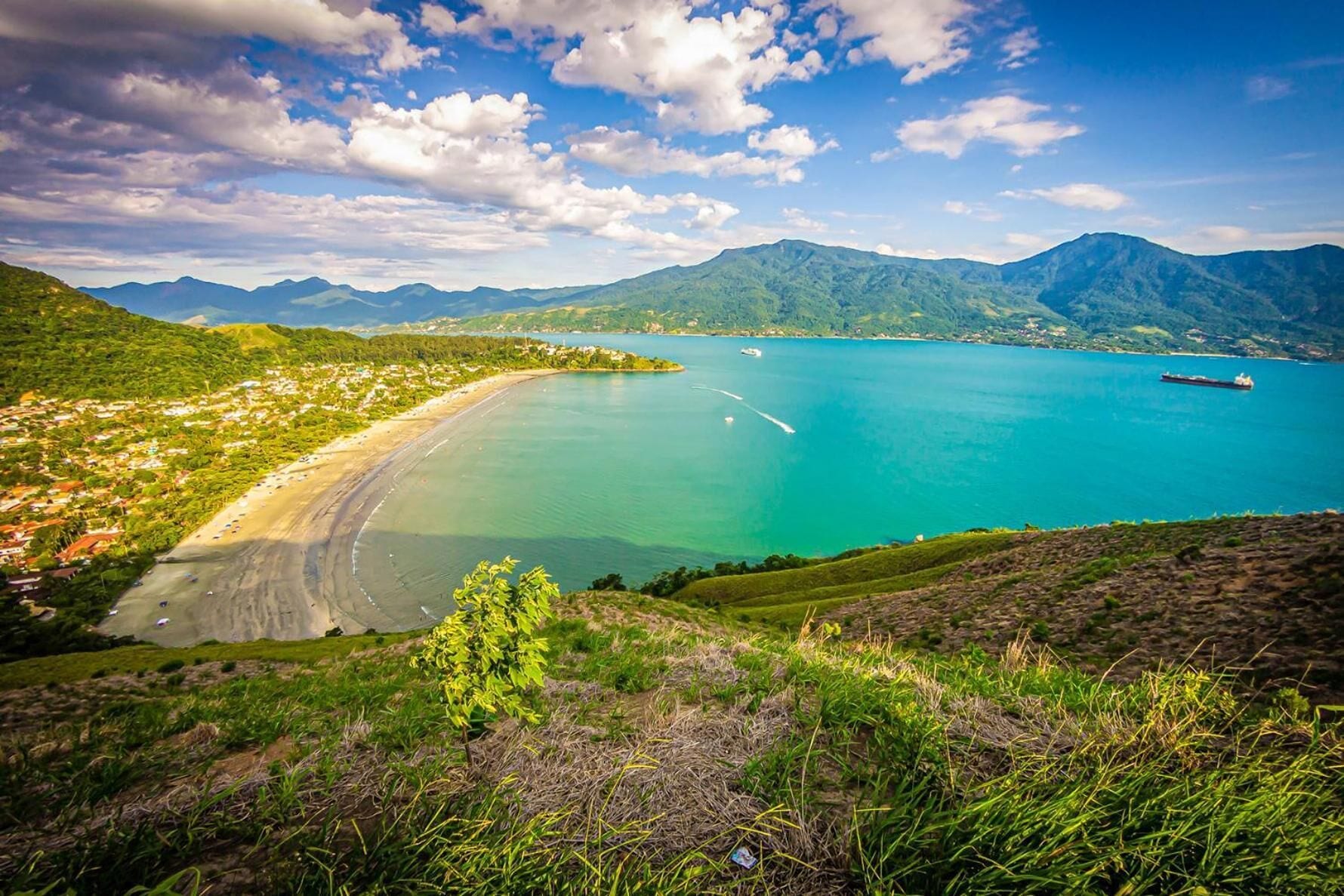 Un paisaje costero con una playa, aguas turquesas cristalinas y montañas al fondo.