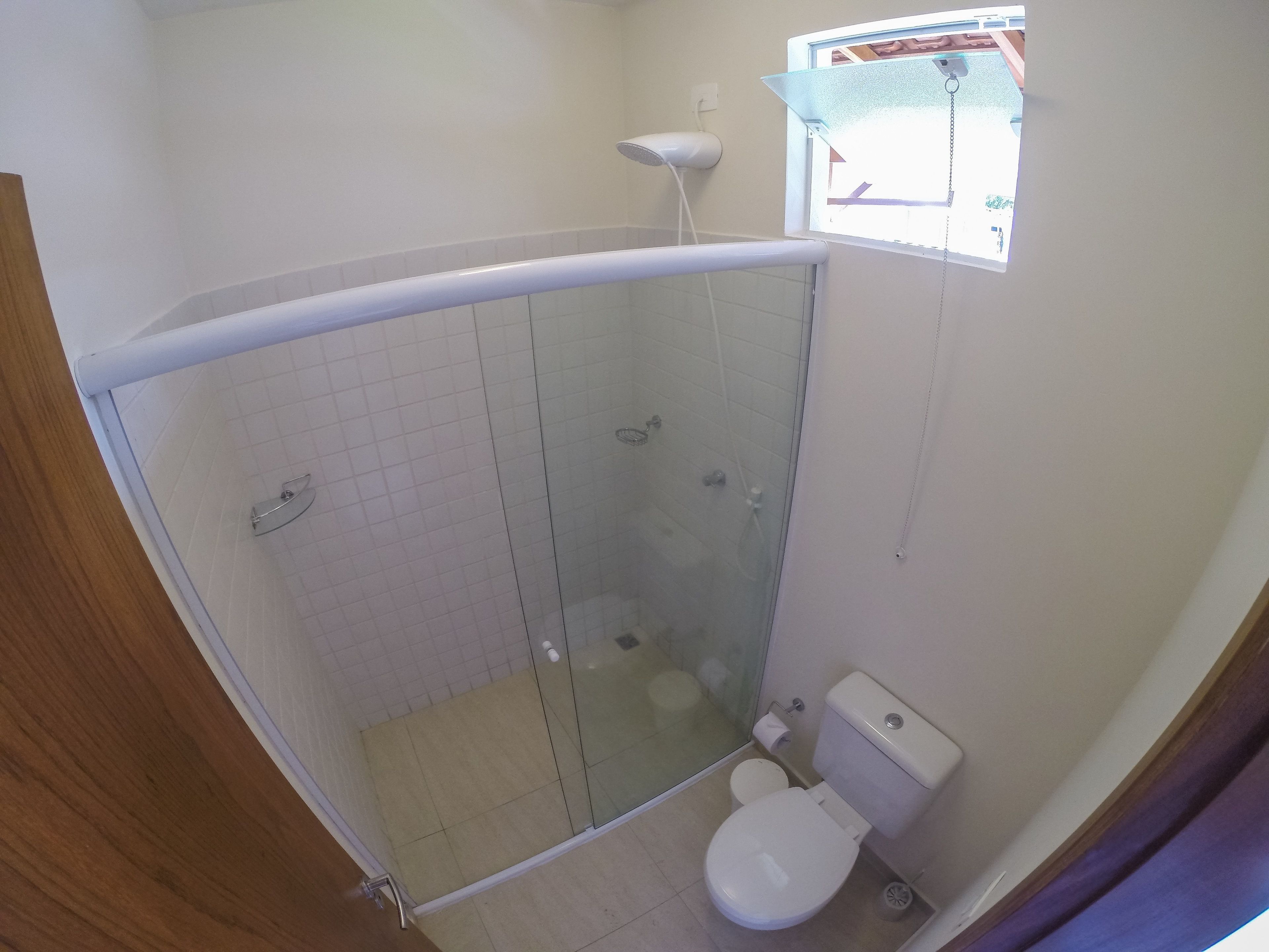A small bathroom with a glass-enclosed shower, a toilet, and a window above the sink.