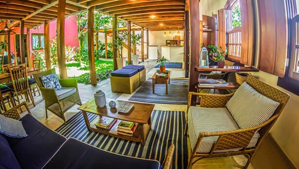 A spacious indoor area with wooden beams, wicker furniture, and a central seating area with a coffee table. - Pousada Ipê (São Sebastião)