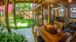 A wooden outdoor dining area with a table set for two, surrounded by chairs, and a large umbrella overhead. - Pousada Ipê (São Sebastião)