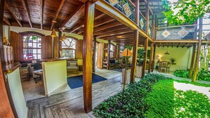 A spacious lobby with wooden beams, a reception desk, seating area, and a garden with greenery. - Pousada Ipê (São Sebastião)