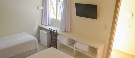 A hotel room with two beds, a desk with a chair, a TV mounted on the wall, and a window with curtains.