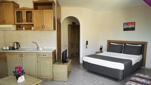 Ein kompaktes Hotelzimmer mit Küchenzeile, einem Bett und einem kleinen Tisch mit Blumenarrangements.
