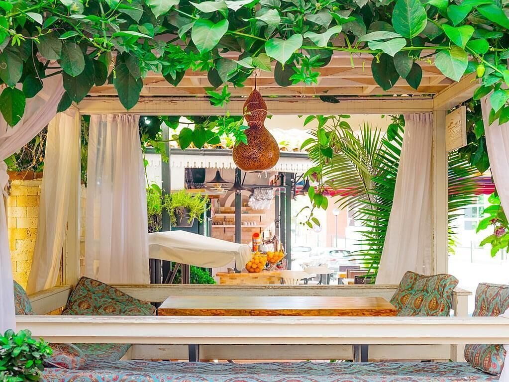 A cozy outdoor seating area with a wooden bench, a hanging light fixture, and lush greenery.