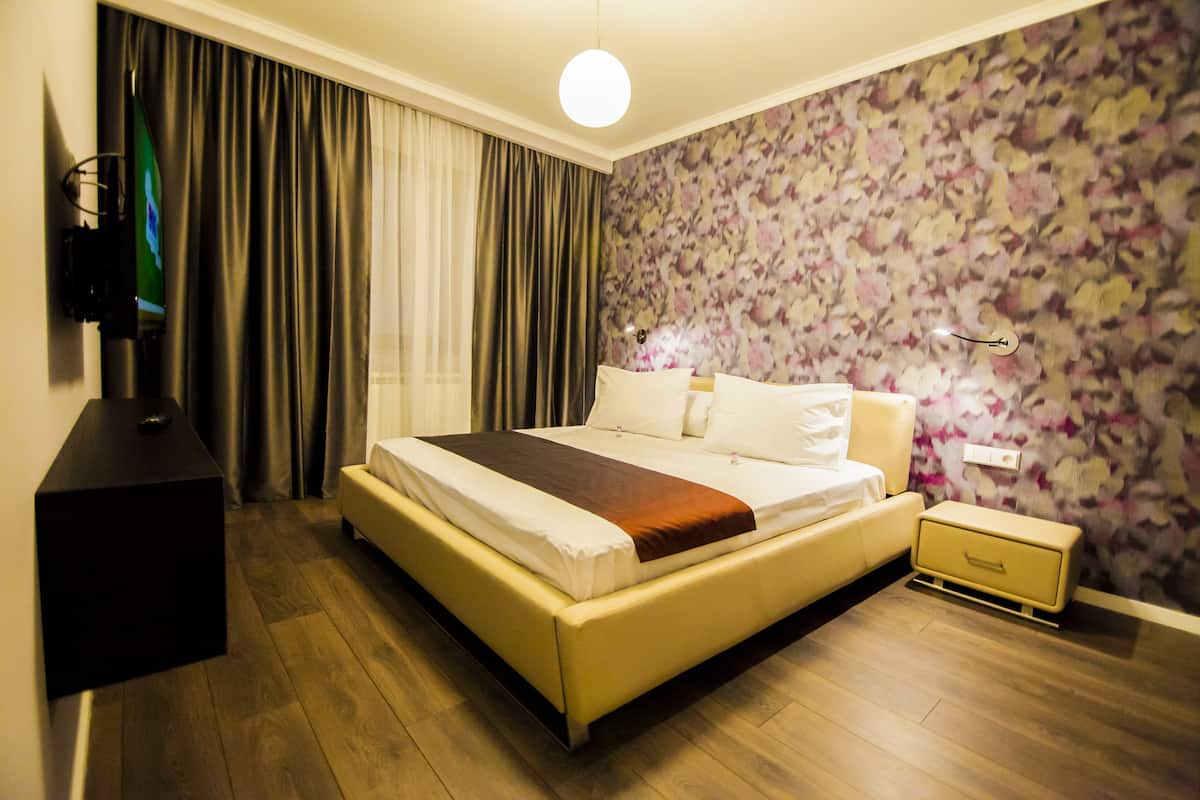 A hotel room with a bed, a nightstand, a TV, and a floral wallpaper.