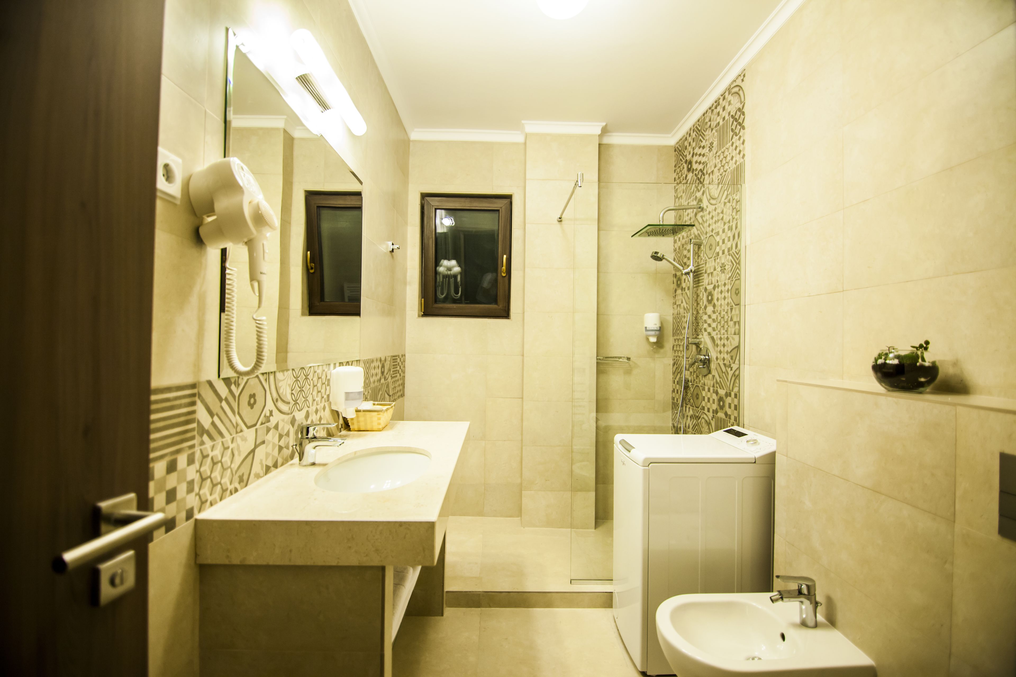 A bathroom with a double sink, a mirror, a hairdryer, a shower, and a small shelf with toiletries.