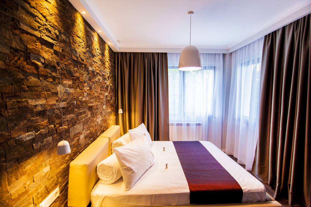 A modern hotel room with a stone wall, a large bed with white bedding, and a hanging pendant light.